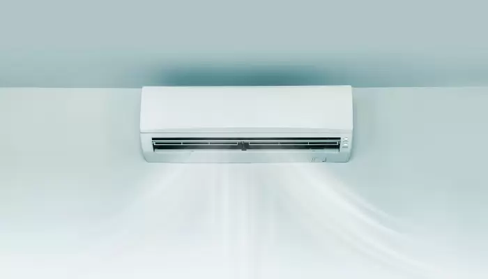 Indoor wall-mounted air conditioning unit emitting cool air from high on light-colored wall