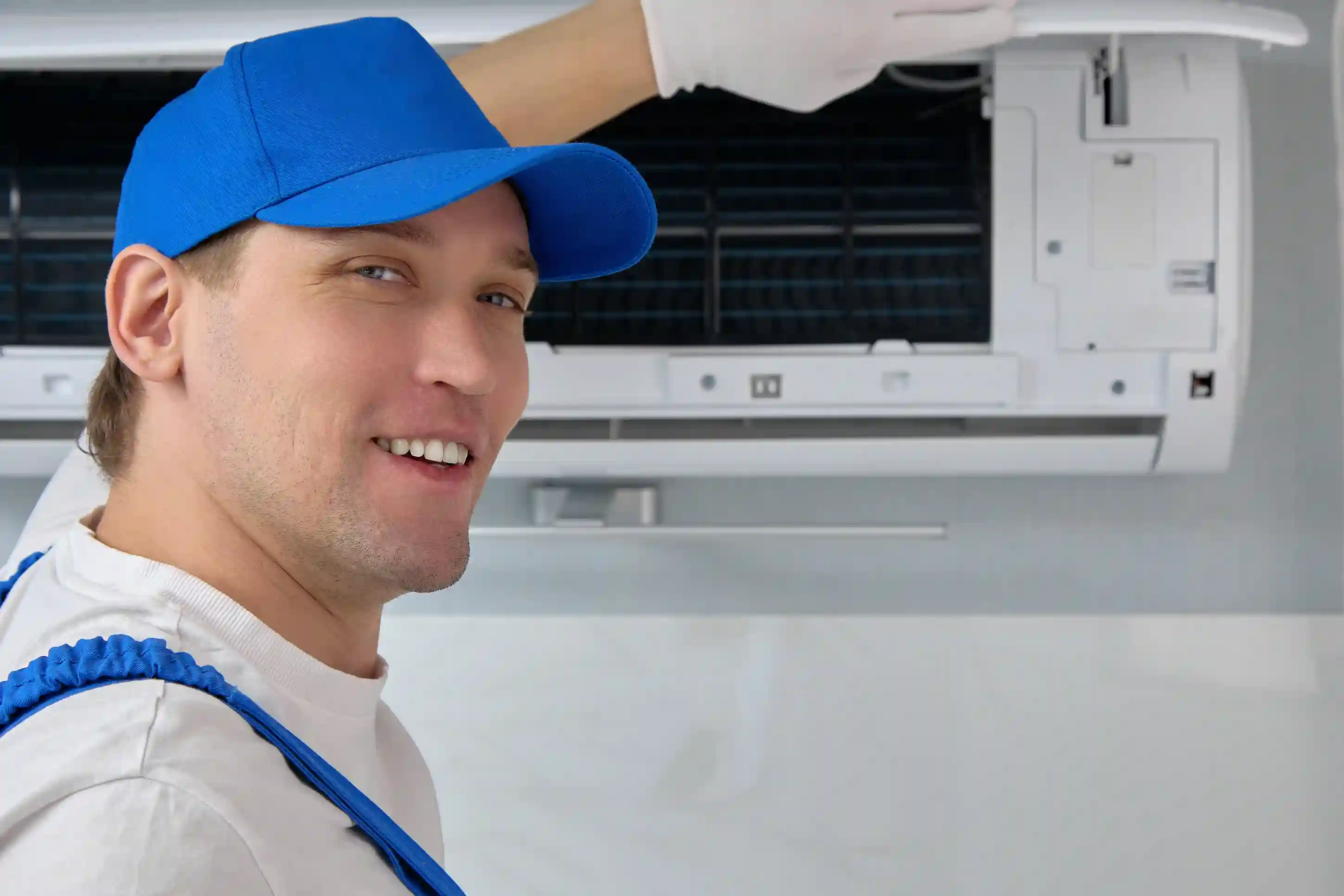 A person smiling back and wearing a blue hat is replacing a ductless AC unit