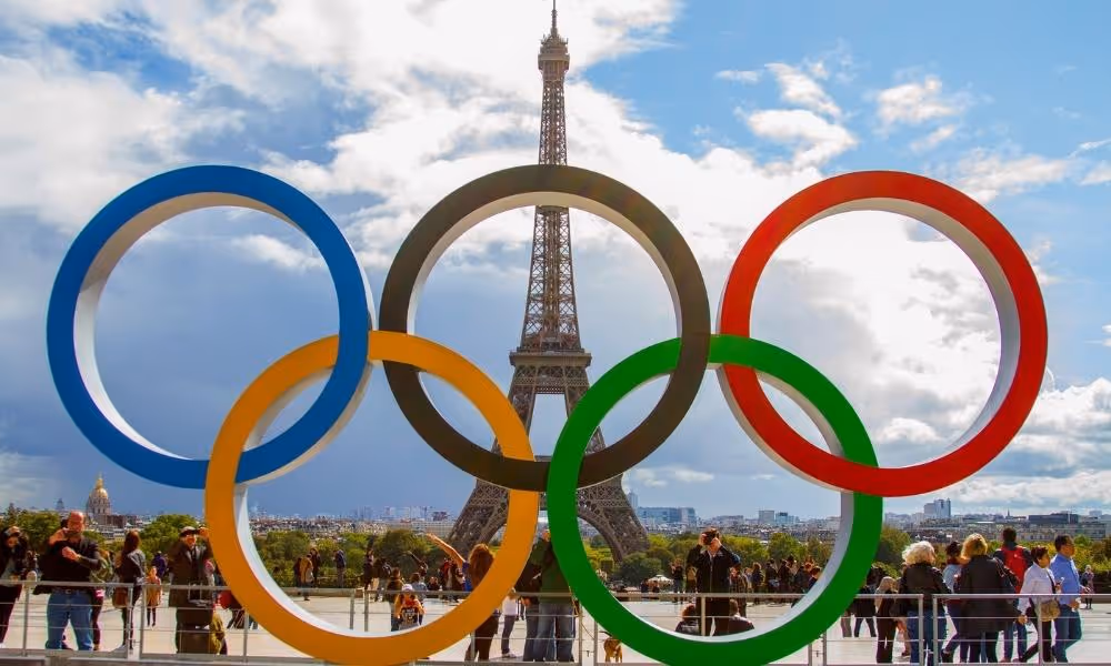 Five colorful Olympic rings, made of recycled French steel, prominently displayed on the Eiffel Tower, symbolizing the excitement and anticipation for the Paris 2024 Olympics, with the iconic landmark serving as a backdrop.