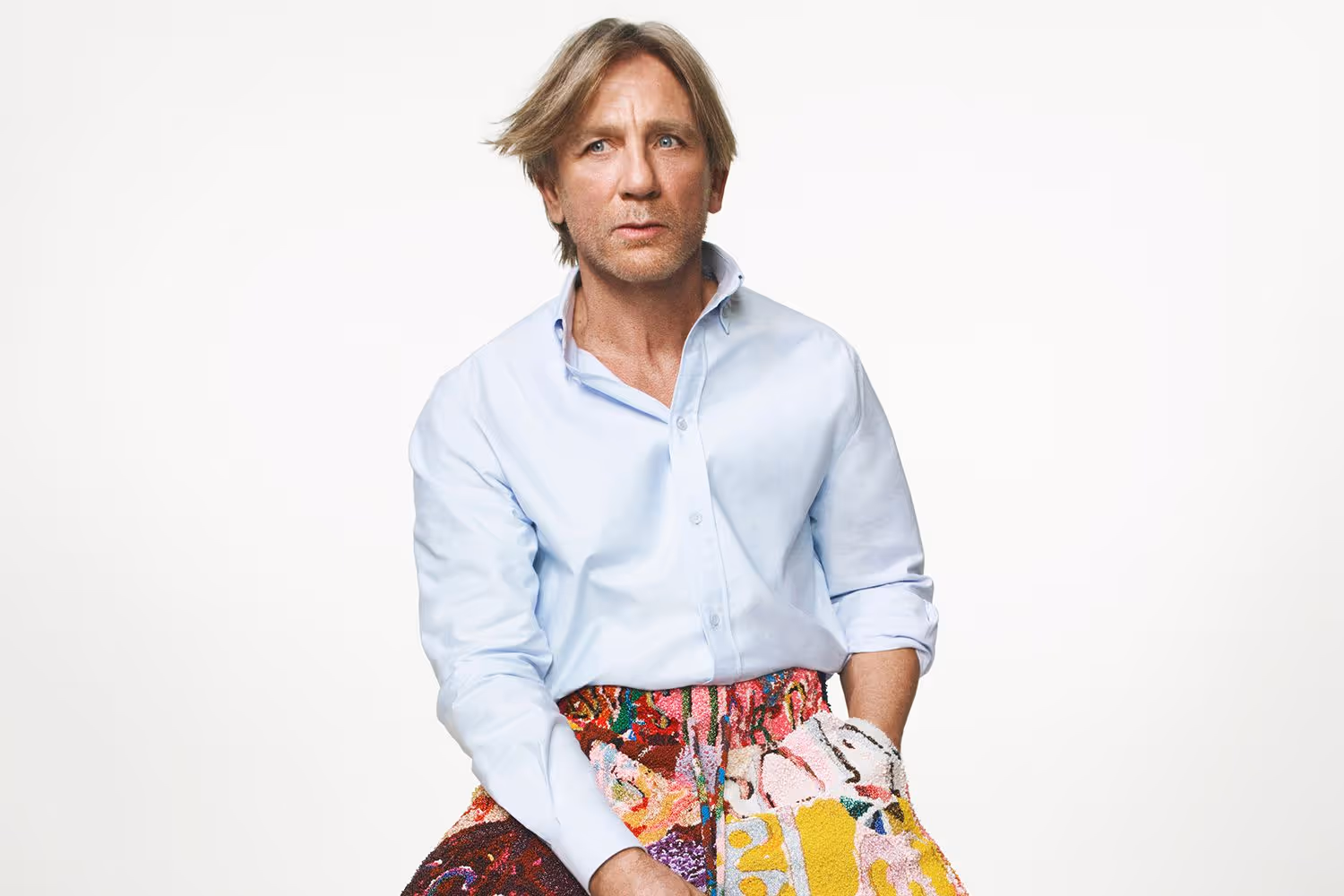 Daniel Craig poses in a vibrant blue shirt paired with colorful patterned pants, showcasing a bold fashion statement for LOEWE.