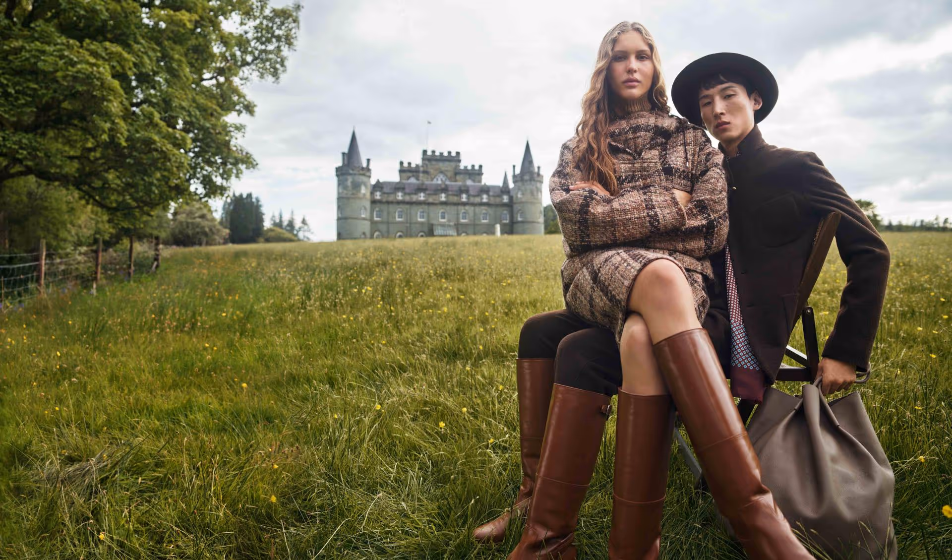 A stylish male and female model seated closely together, exuding elegance and intimacy while wearing Loro Piana's luxurious cashmere garments, set against a scenic backdrop that reflects the brand's heritage and celebration of 100 years in luxury fashion