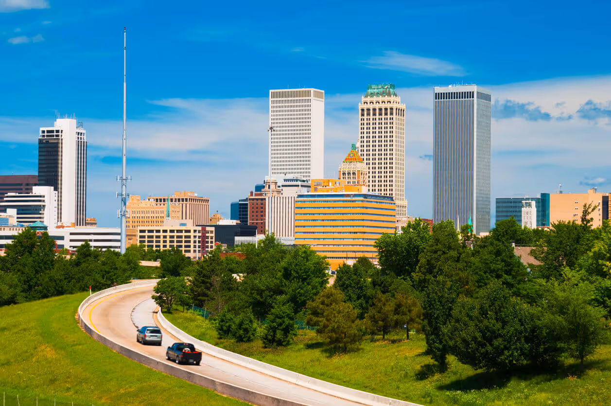 Tulsa skyline with modern skyscrapers, green trees, and curved highway