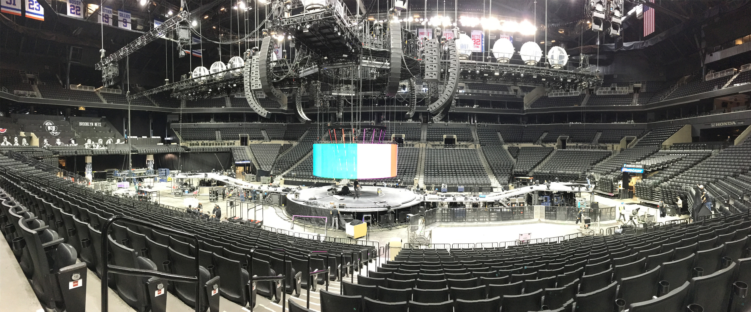 A panoramic shot of a stage with a large sound system in the middle of an empty arena.