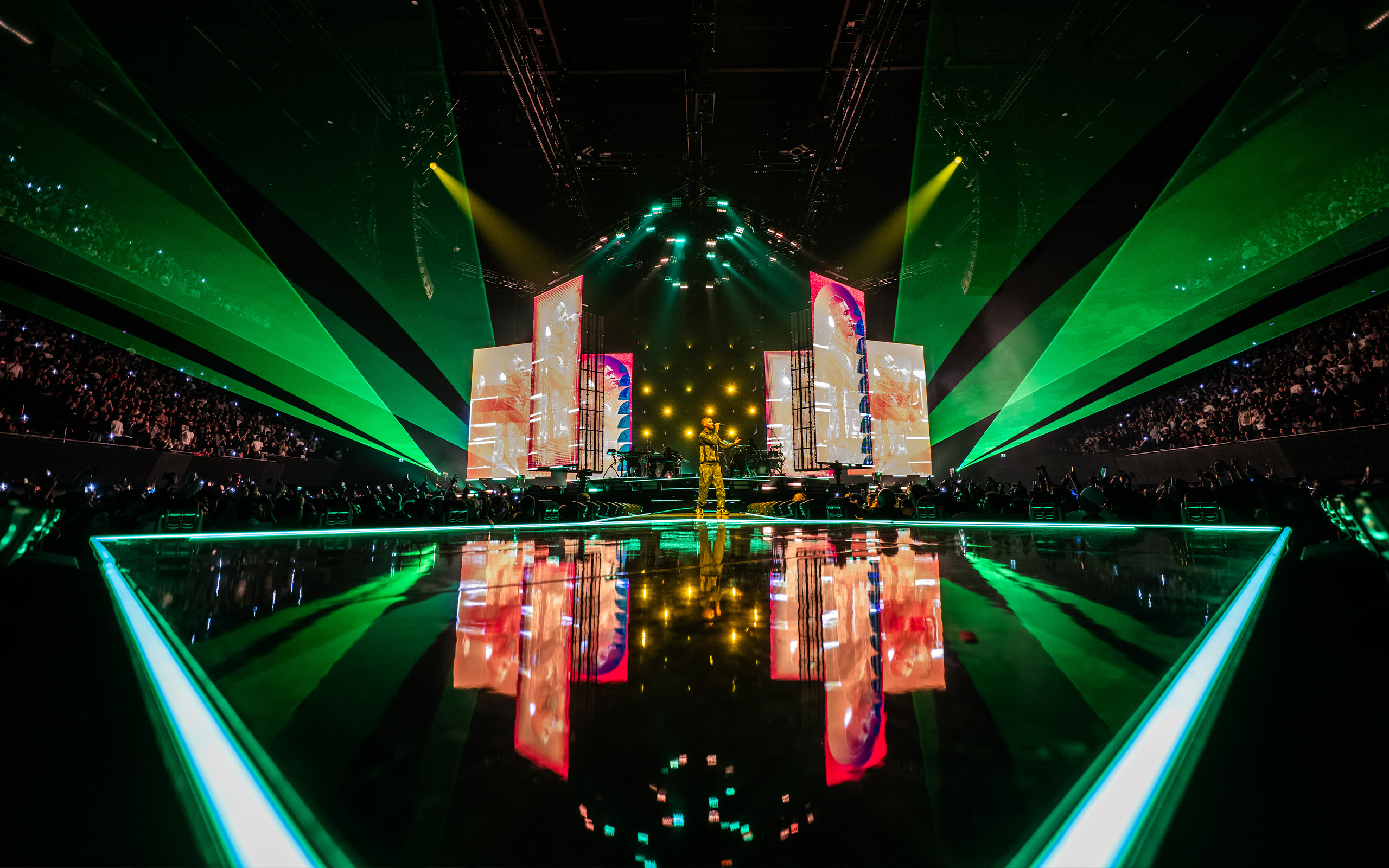 A wide shot from the front of the stage of Dave performing in front of green lasers and lights