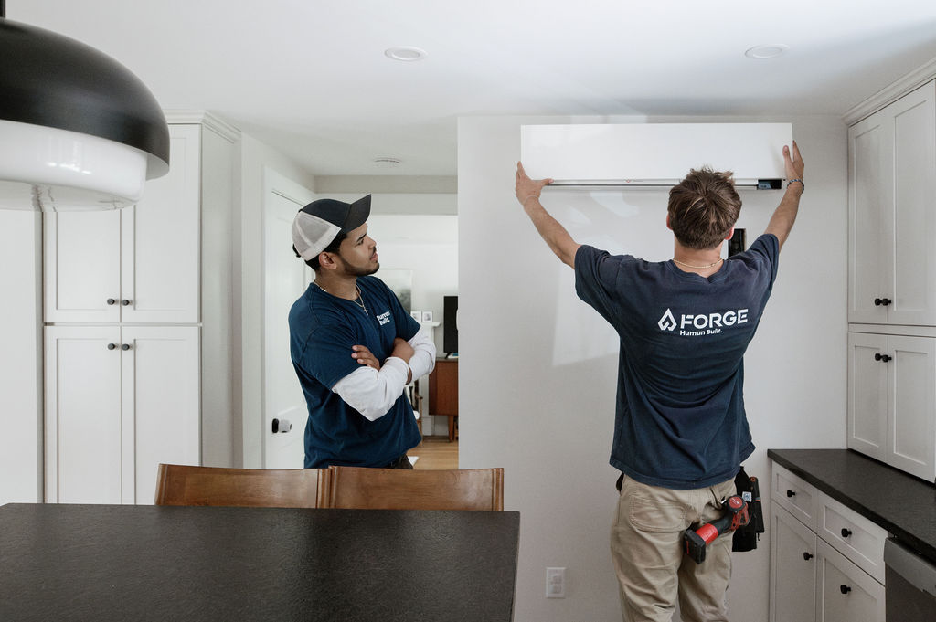 Two Forge installers fitting an indoor mini split head on a kitchen wall