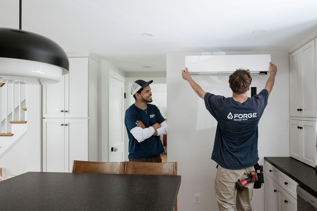 Two Forge installers setting an indoor heat pump head unit on a kitchen wall