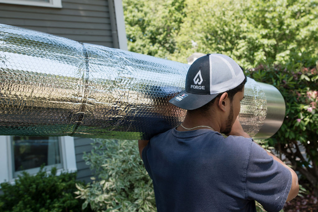 A Forge installer carrying insulated duct along the side of a house