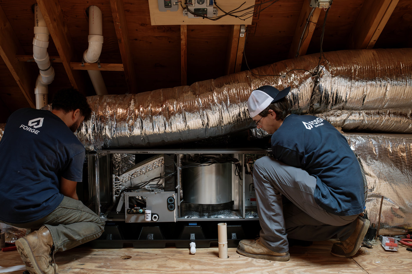 Two Forge installers setting an air handler into the attic ductwork