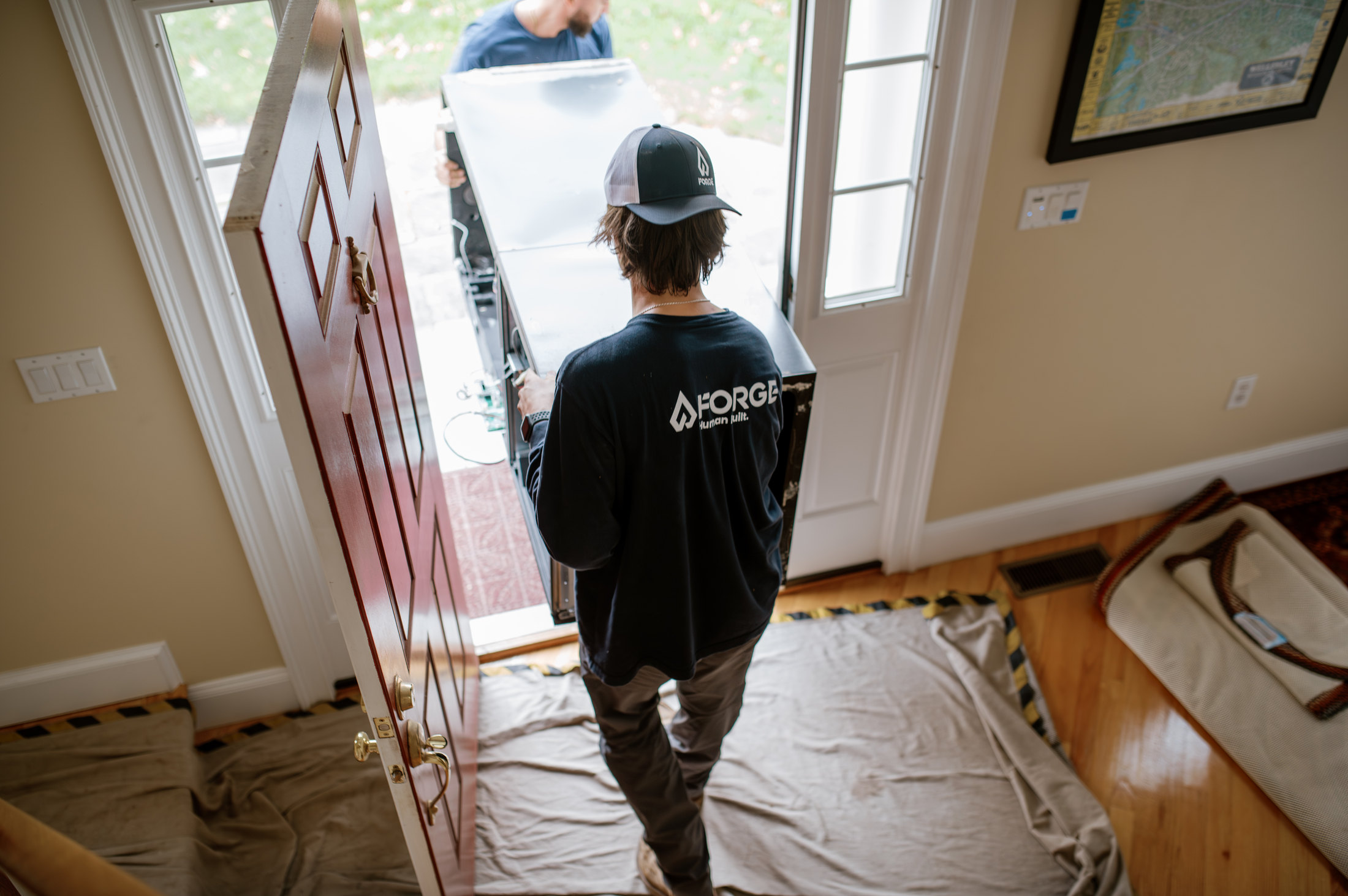 A Forge crew member carrying equipment into a home over drop cloths