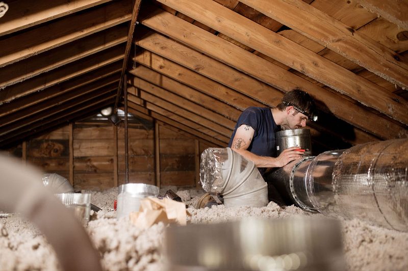 A Forge installer fitting ductwork in an insulated attic