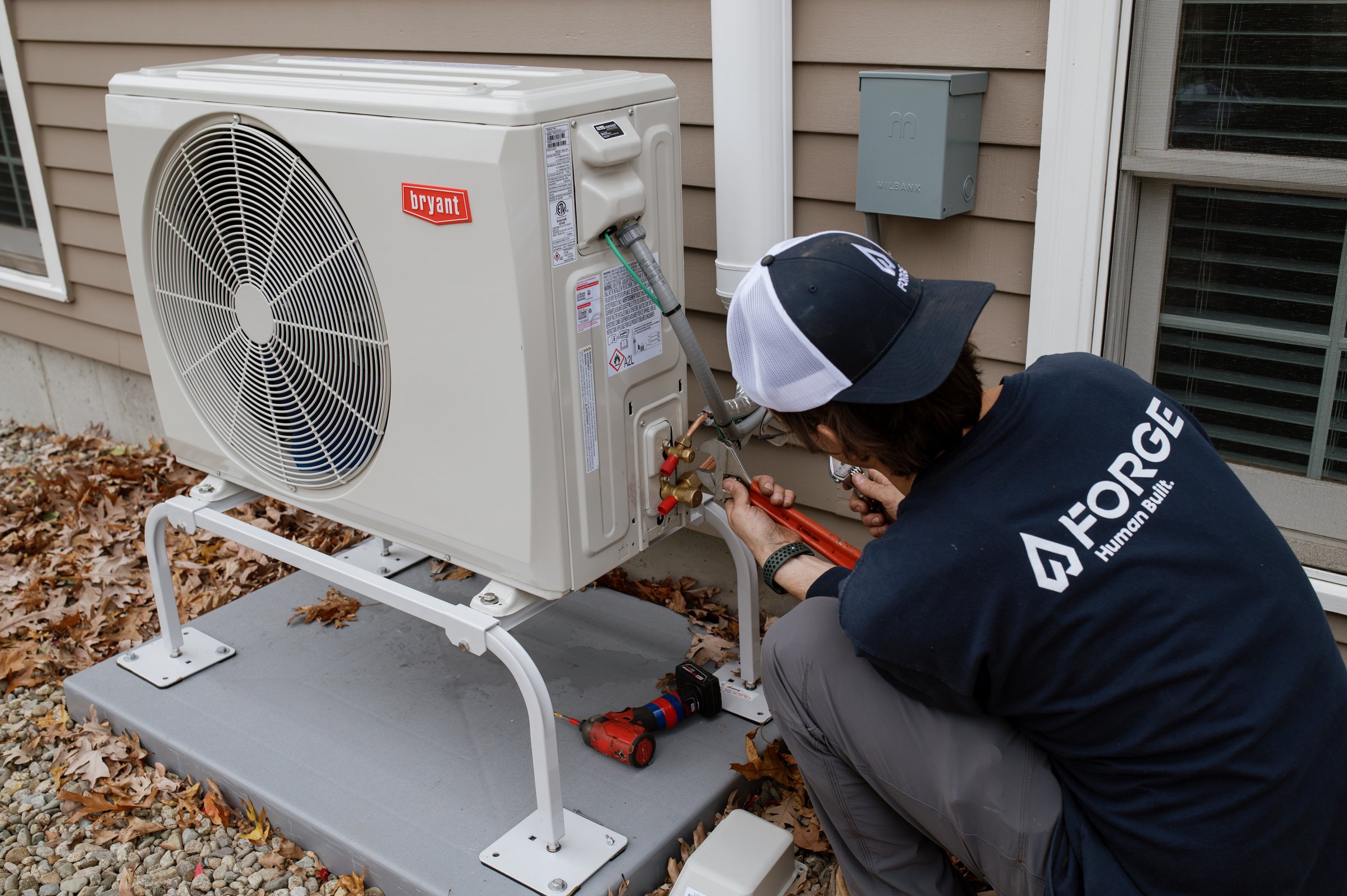 Forge installer connecting refrigerant lines on a Bryant outdoor heat pump unit at a Massachusetts home
