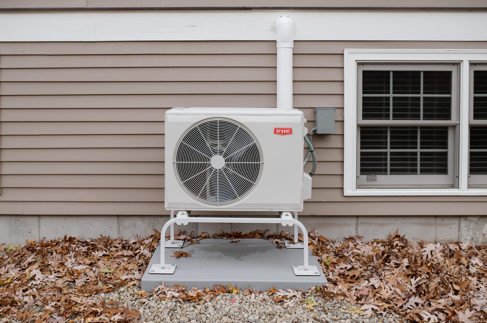 A cold-climate outdoor heat pump unit on a stand beside a Massachusetts home