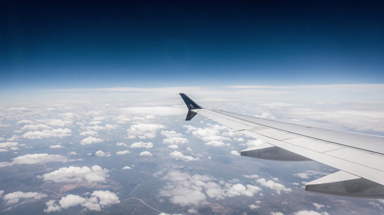 The image depicts the wing of a Bombardier Global 7500 business jet soaring above a sea of clouds during a long-range cruise, showcasing its sleek design and exceptional performance in the sky. The view emphasizes the aircraft's impressive altitude and the vast expanse of blue sky surrounding it.