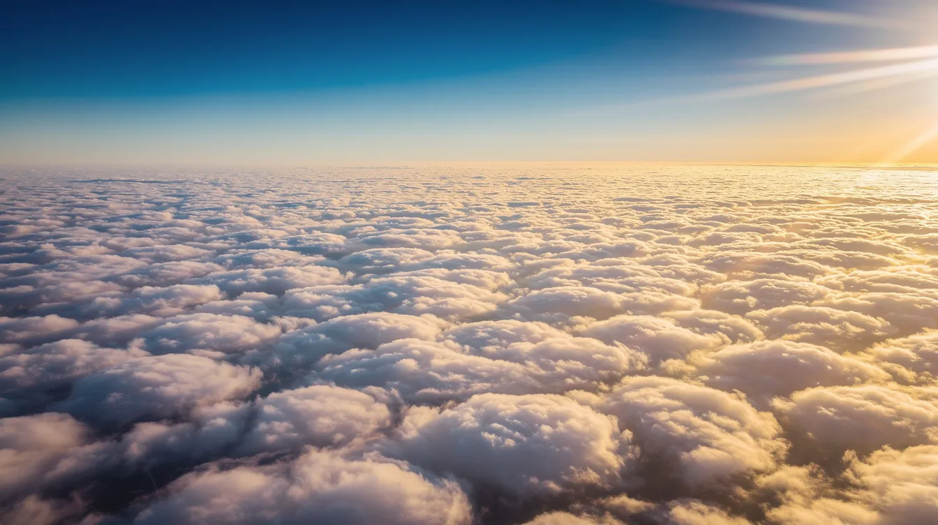 The image depicts a breathtaking view from high altitude above a thick layer of white clouds, with a vibrant blue sky and sunlight streaming across the horizon. This scene captures the upper atmosphere where jet stream winds flow, highlighting the beauty of the Earth's weather systems and the interplay of warm and cold air masses.