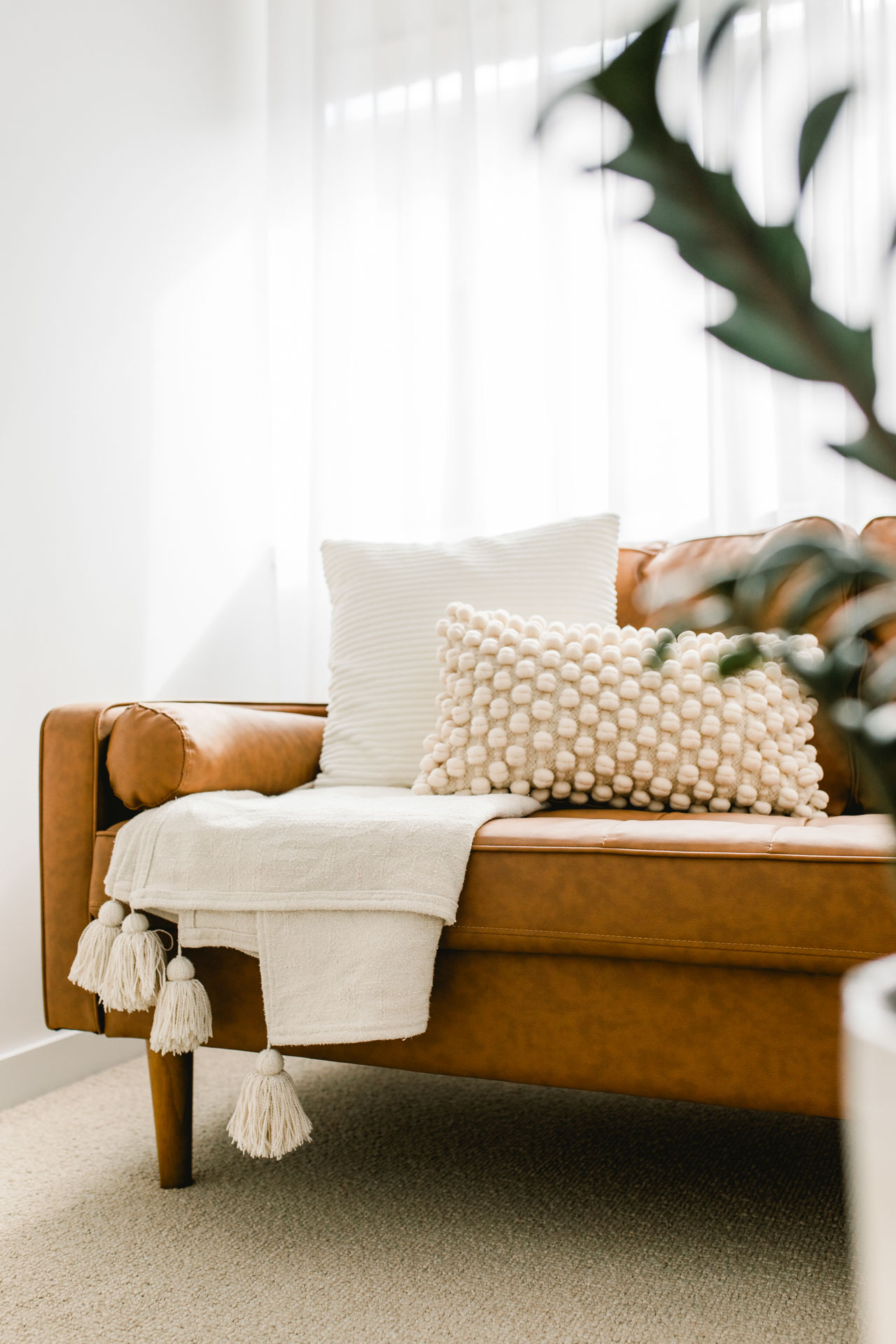 A cozy brown leather couch with decorative pillows and a green plant in a white vase nearby.