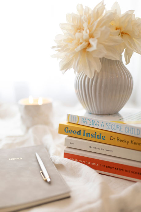 A charming display of  books, a notebook with a pen in it, an elegant flower, and a lightened candle, all placed on a table.