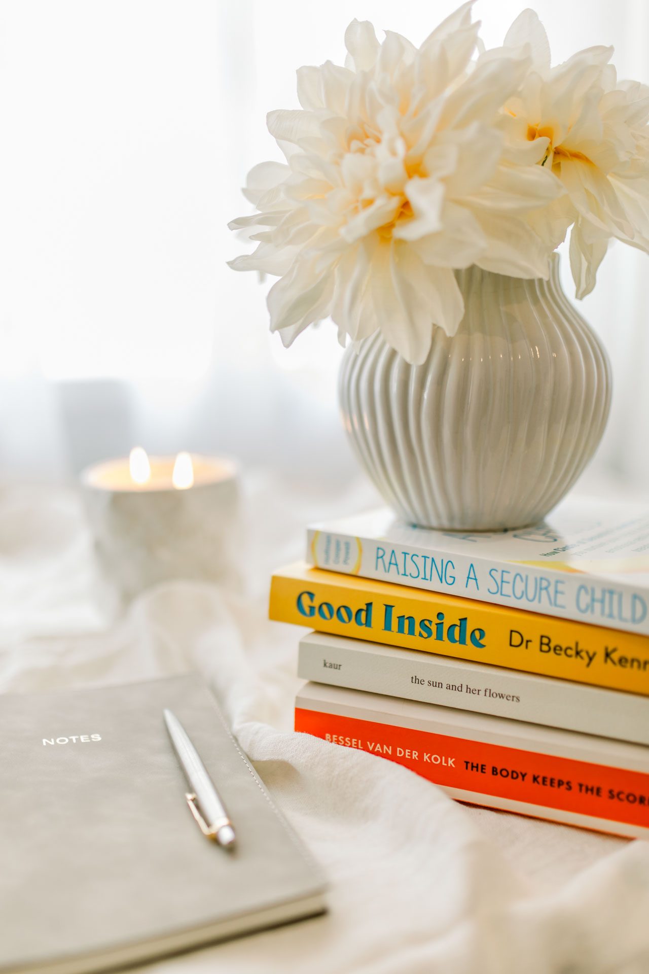 A charming display of  books, a notebook with a pen in it, an elegant flower, and a lightened candle, all placed on a table.