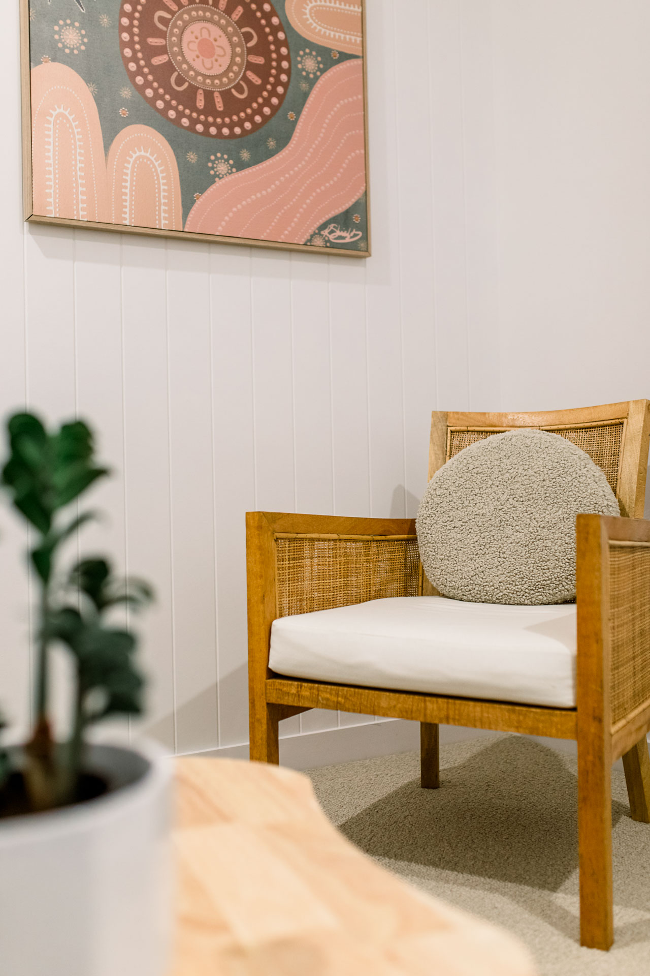 A cozy room with a chair, a green plant, and a vibrant painting hanging on the wall.
