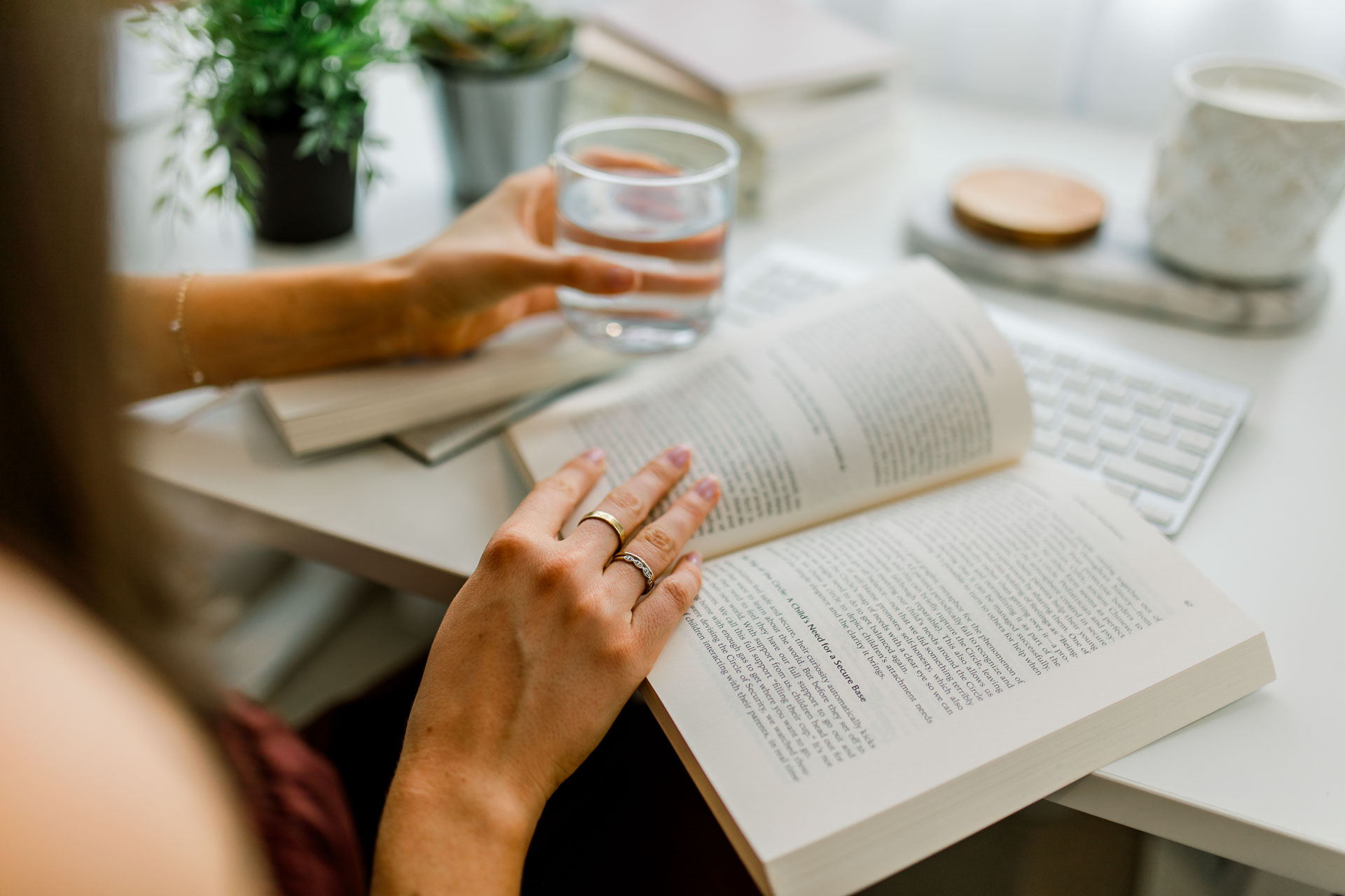 A woman enjoys reading a book, holding a glass of water in her other hand in an elegant displayed table setting.