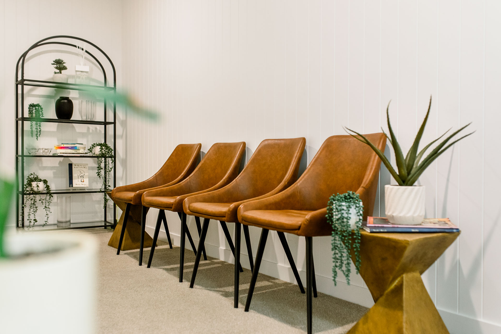 Neatly arranged brown leather chairs at Kiah Place, with a black steel divider with plants on one side and a wooden stand with elegant flowers on the other.