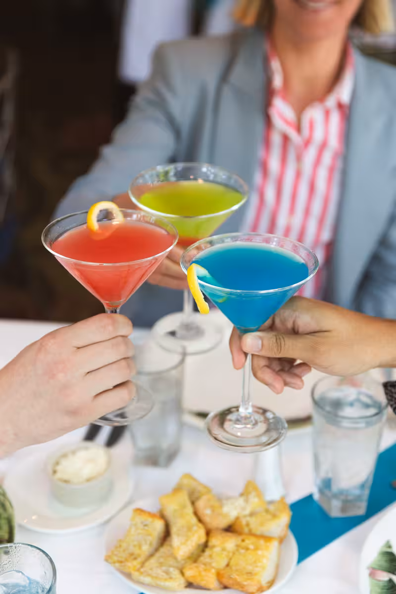 people "cheers" at a table with 3 colorful martinis