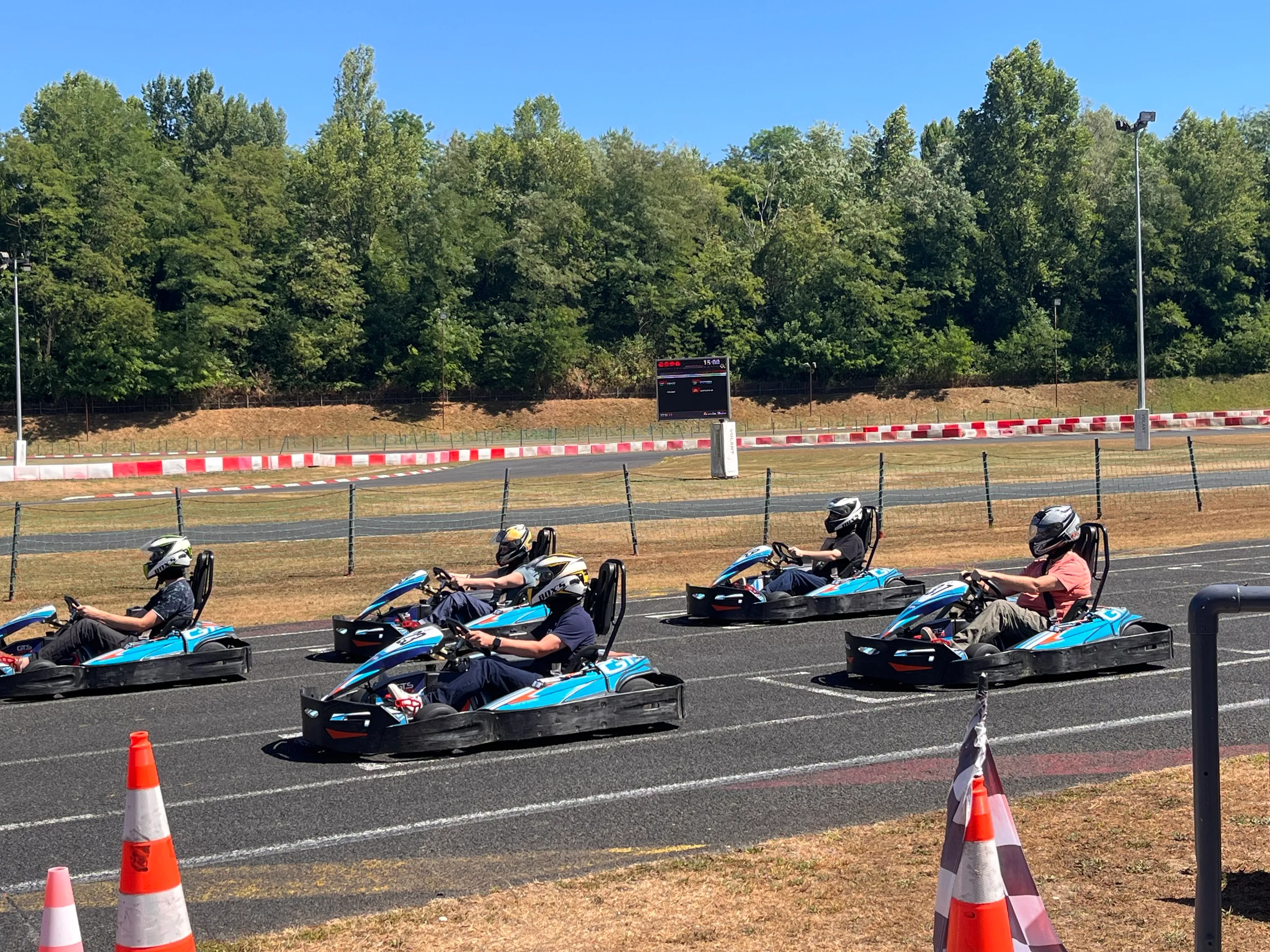 Quatre personnes en casque conduisent des karts bleus sur une piste de karting en plein air.