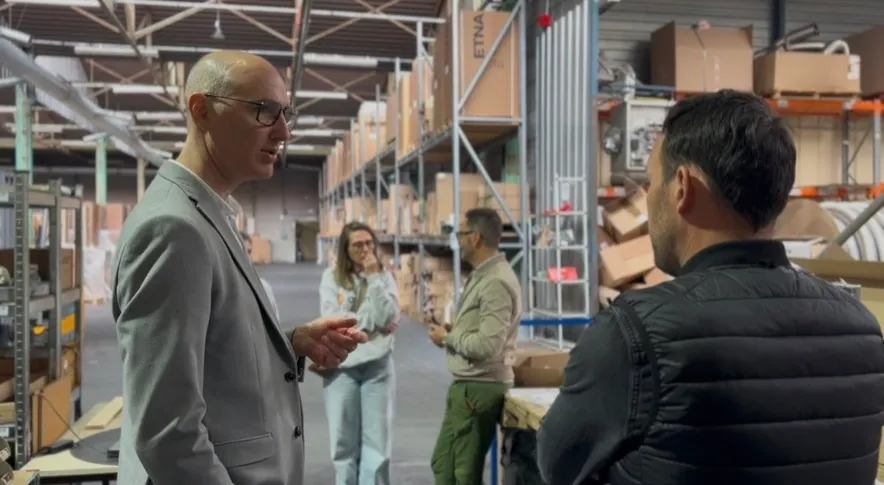 Quatre personnes discutent dans un entrepôt avec des étagères remplies de cartons en arrière-plan.