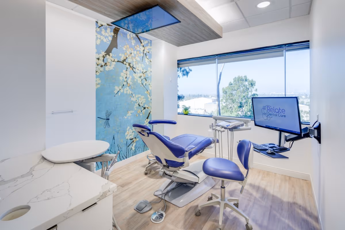 Modern dental exam room with purple dental chair, monitors, and a window showing outdoor greenery.