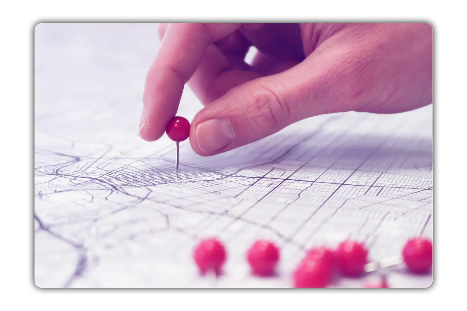 Hand placing a red pushpin on a detailed city map with several other pushpins nearby.