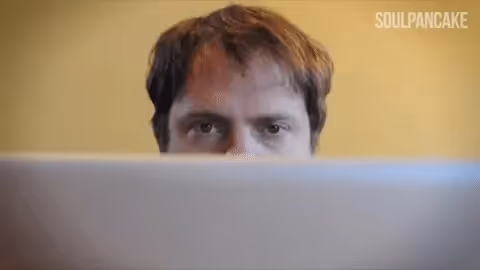 Rainn Wilson looking bored while working behind a laptop