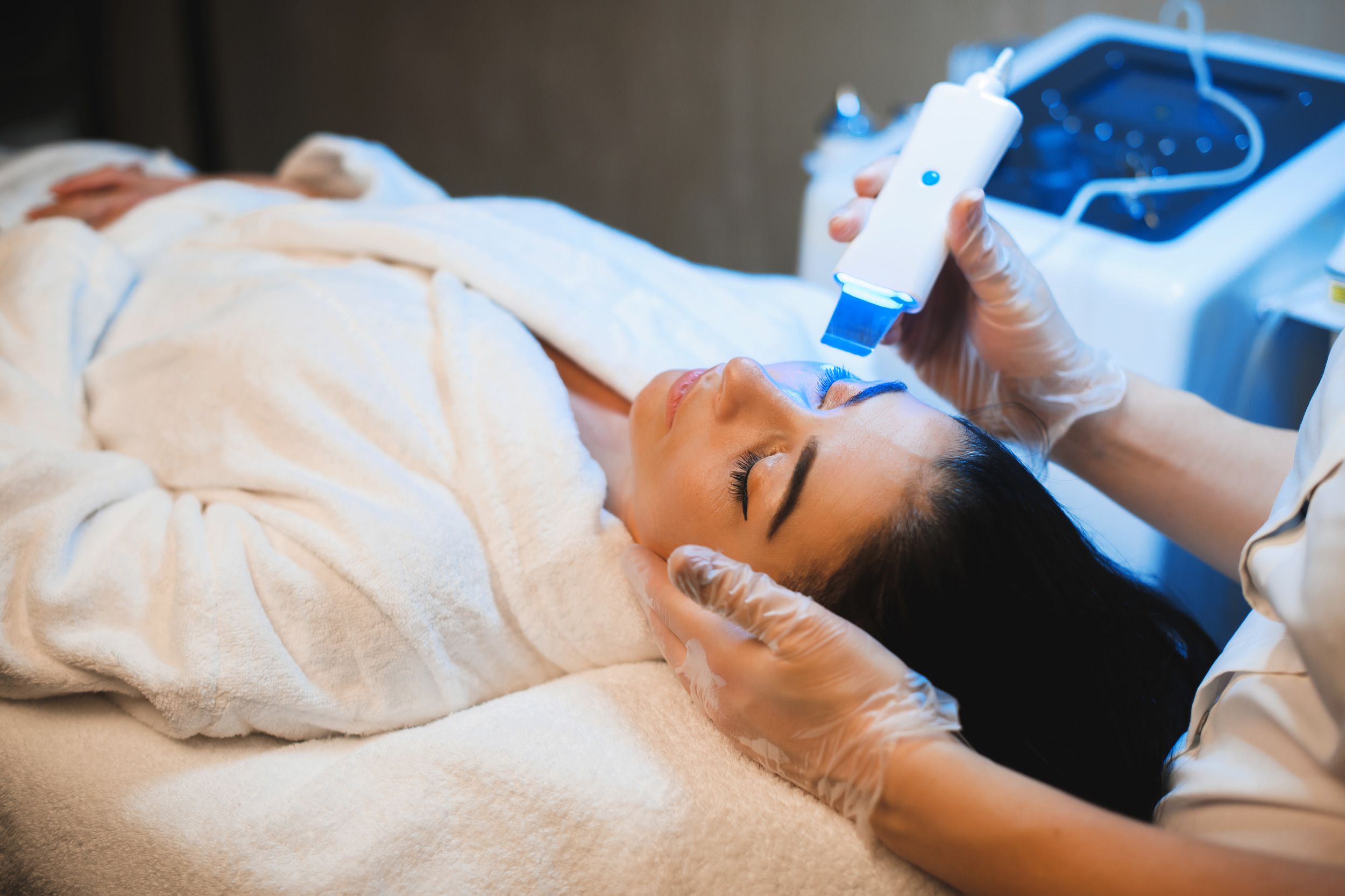 Femme brune subissant un traitement facial laser relaxant pour le rajeunissement dans un spa.