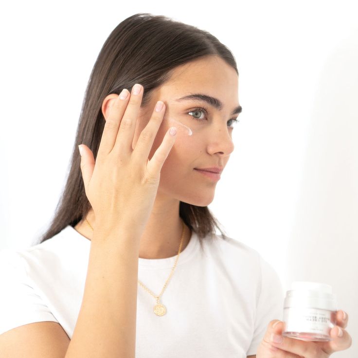 A woman applying eye cream to her face to get rid of eye bags and reduce puffiness. She is using a gentle skin care routine to maintain healthy and youthful-looking skin.