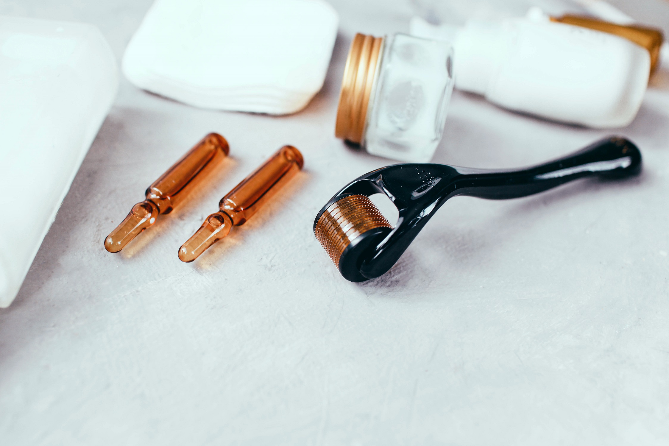Un gros plan d'un dermaroller, d'un sérum et d'une crème anti-âge, utilisés dans un traitement de microneedling pour améliorer la régénération de la peau.