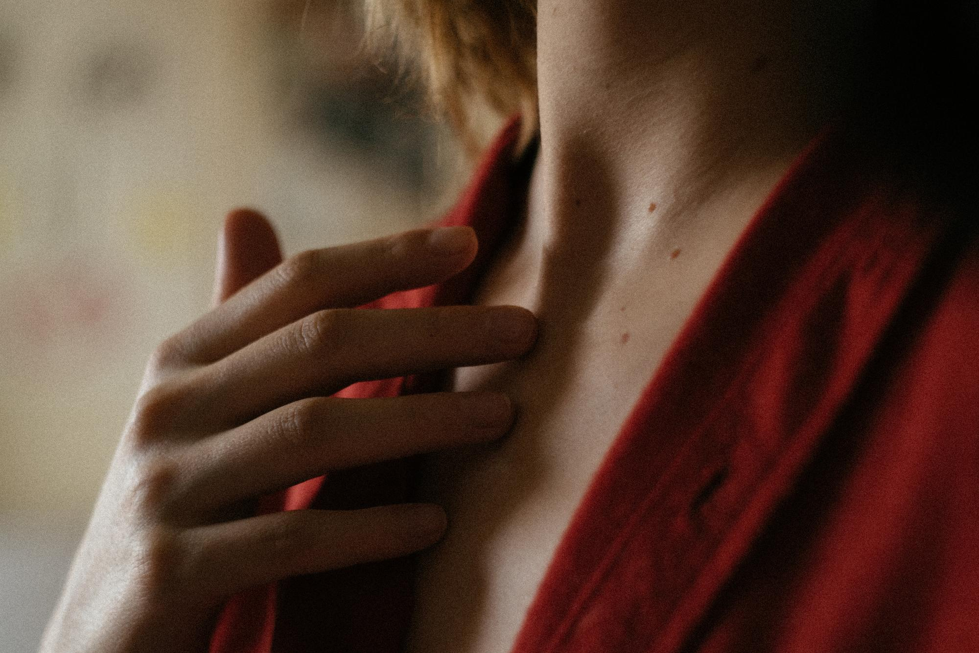 Femme vêtue de rouge touchant son cou et sa poitrine où sont visibles plusieurs petits angiomes rubis sur la peau claire.