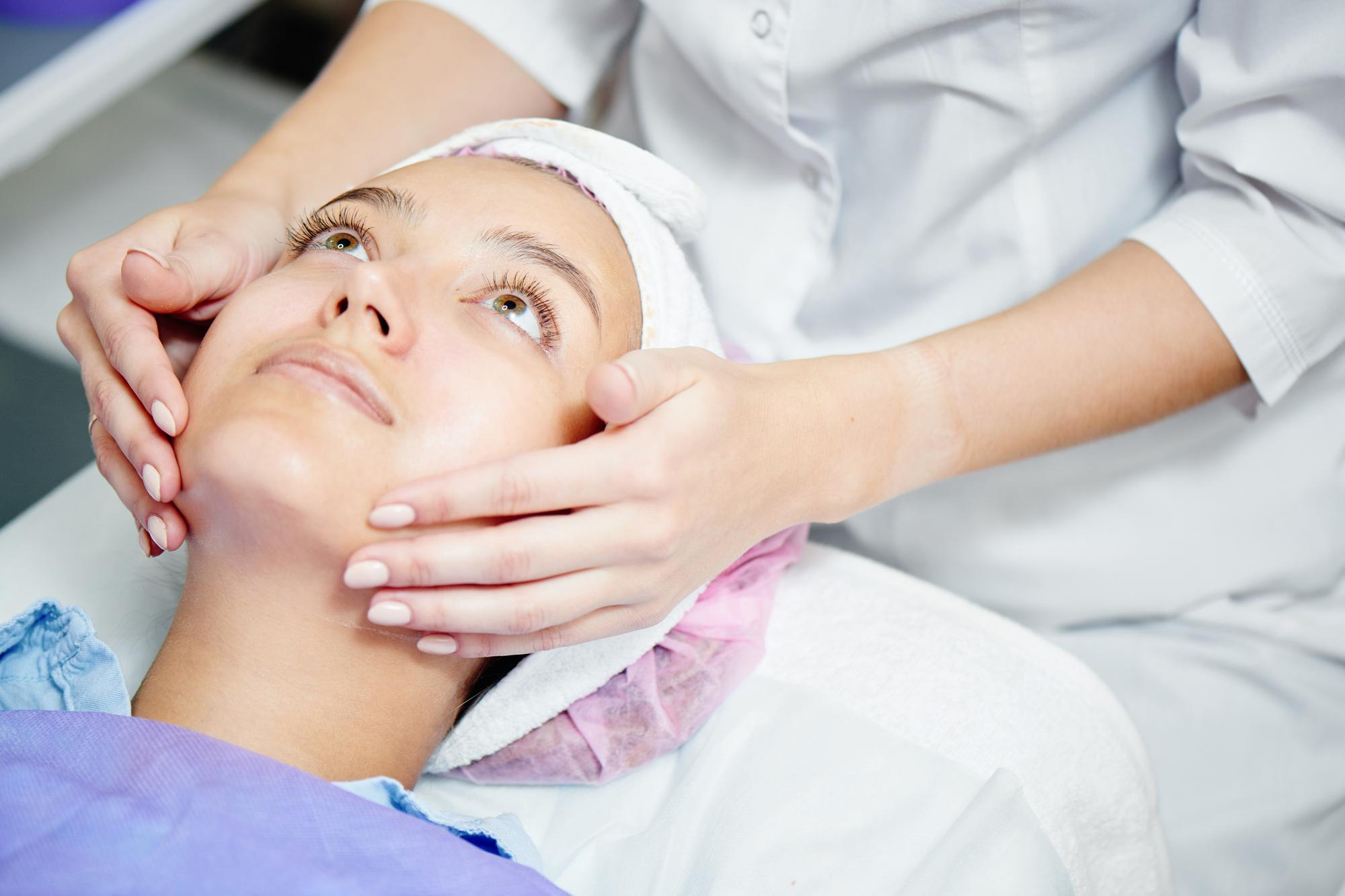 Professionnelle en blouse blanche réalisant un traitement des rides du visage sur une patiente allongée portant un bonnet rose.