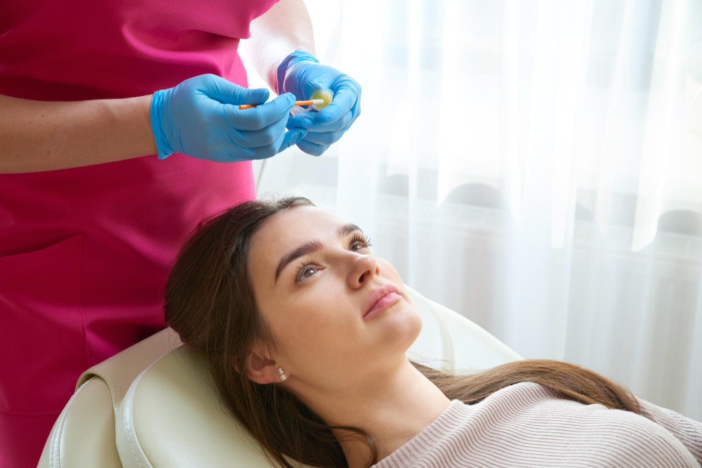 Professionnelle préparant une fiole de traitement pendant qu'une cliente attend, tête inclinée.