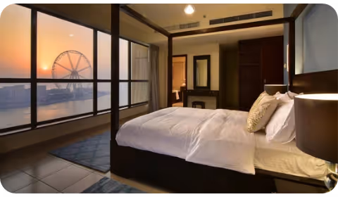Photo of a bedroom in Dubai looking out into JBR when the sun is setting, with a view of the ferry’s wheel