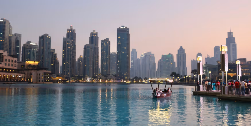 Photo of the Dubai Skyline by the Dubai Mall where you can see a man-made lake, and the buildings in the background