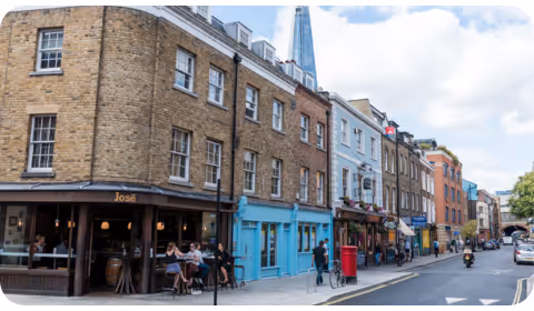 Bermondsey High Street with people sat in terraces and the tip of the shard showing behind the brown stone buildings