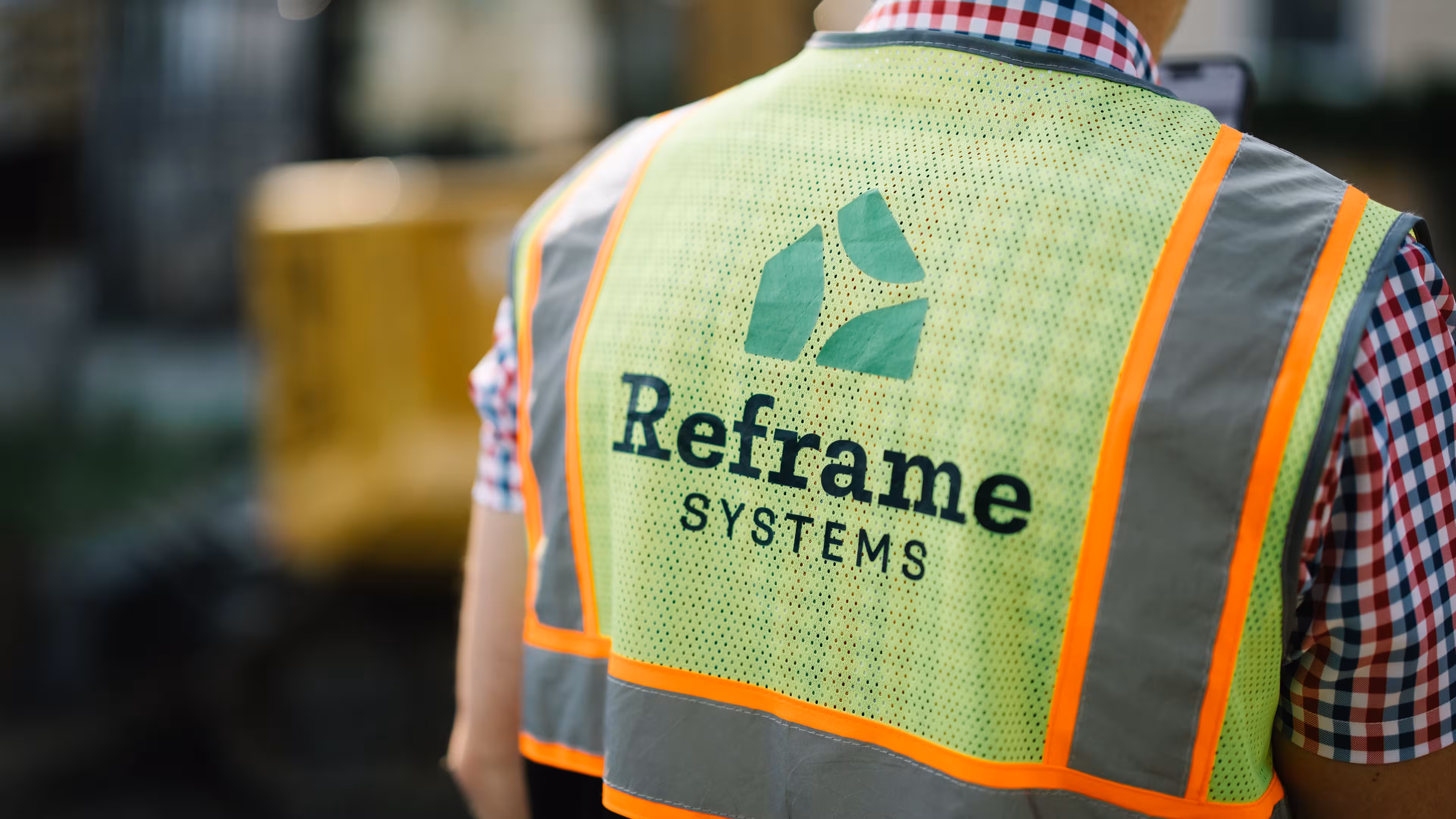 Worker in a Reframe Systems high-visibility safety vest at an industrial build site