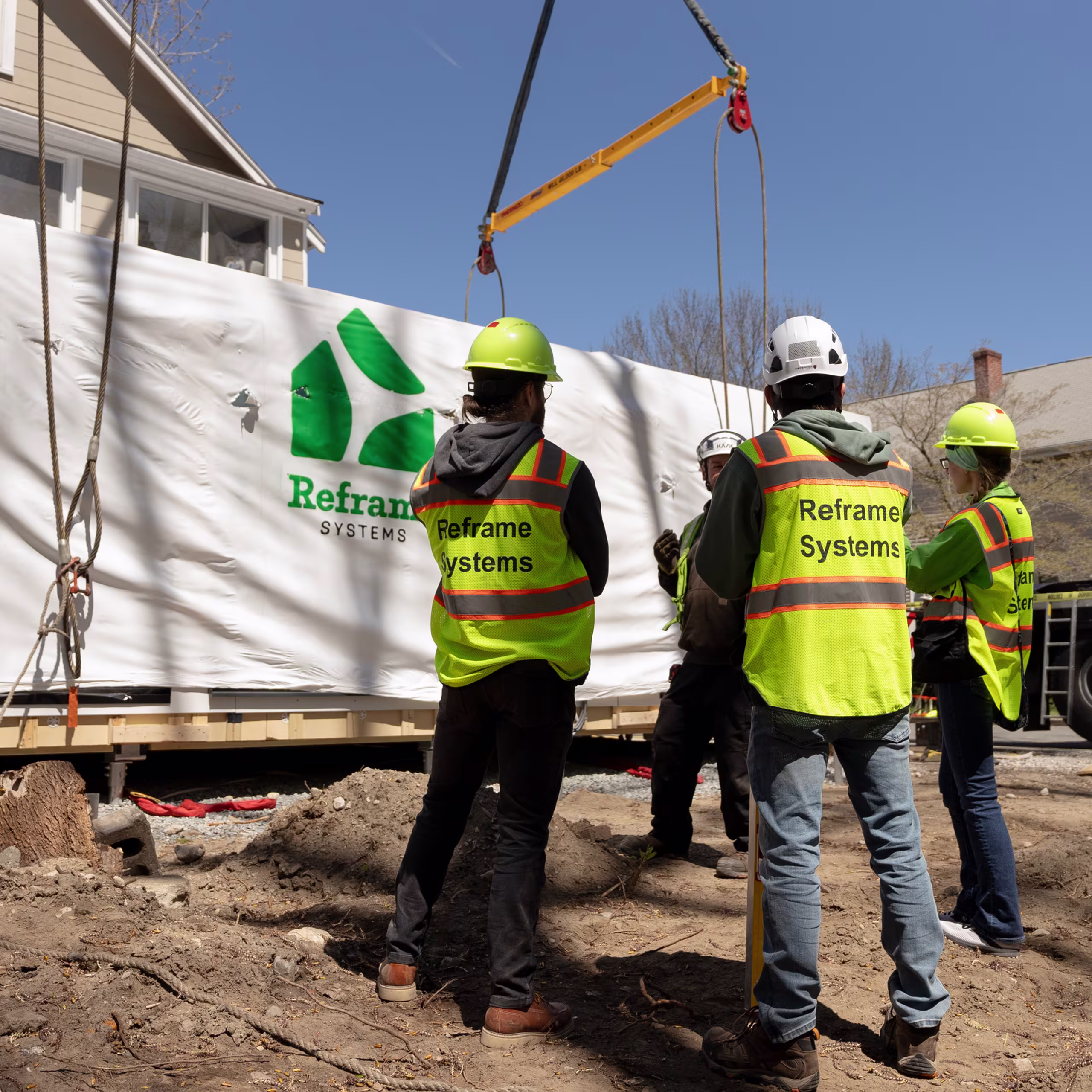 Reframe Systems crew guiding a crane-lifted home module at an outdoor site