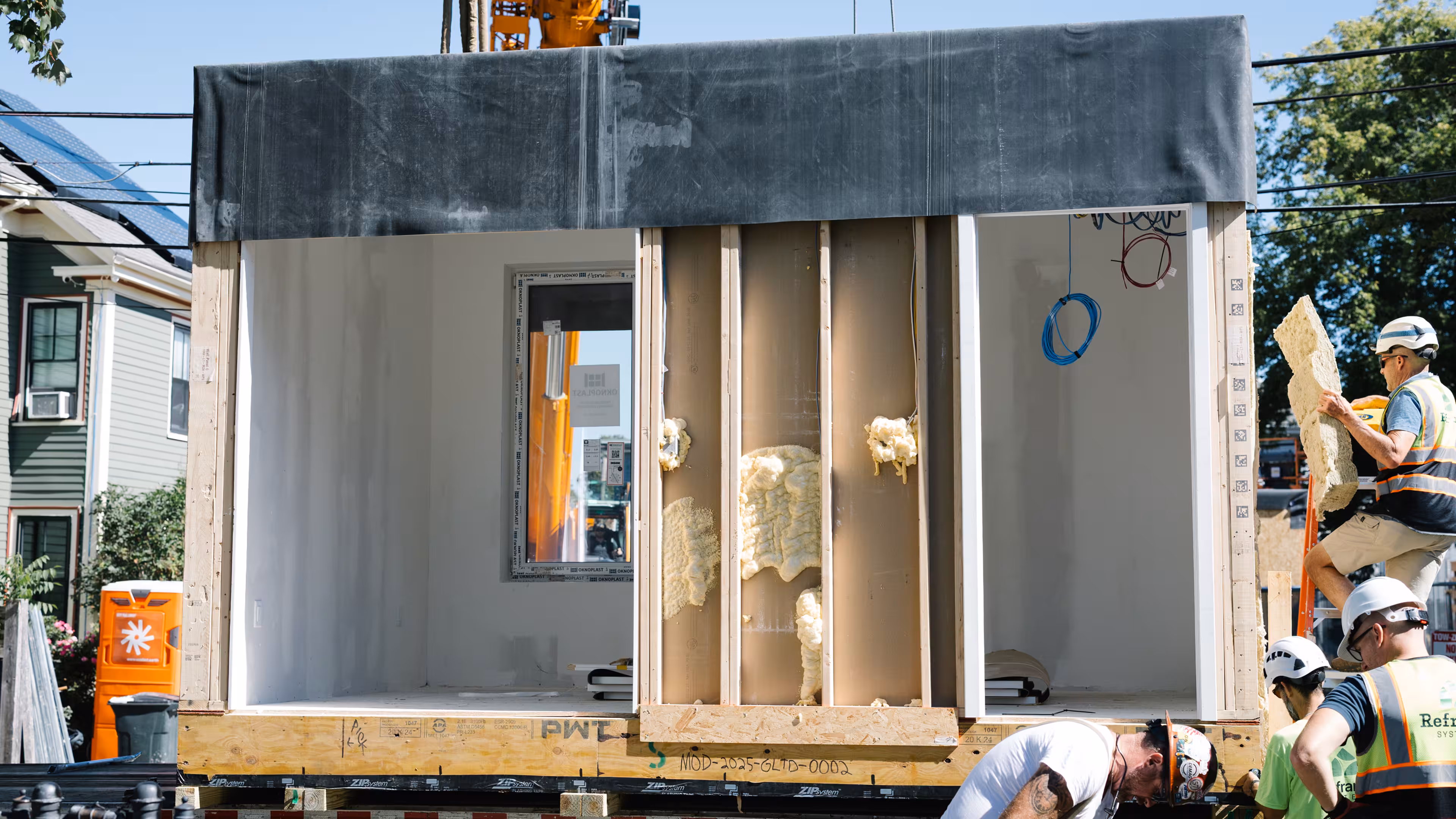 Crane lifting a prefabricated Reframe Systems home module onto a residential street