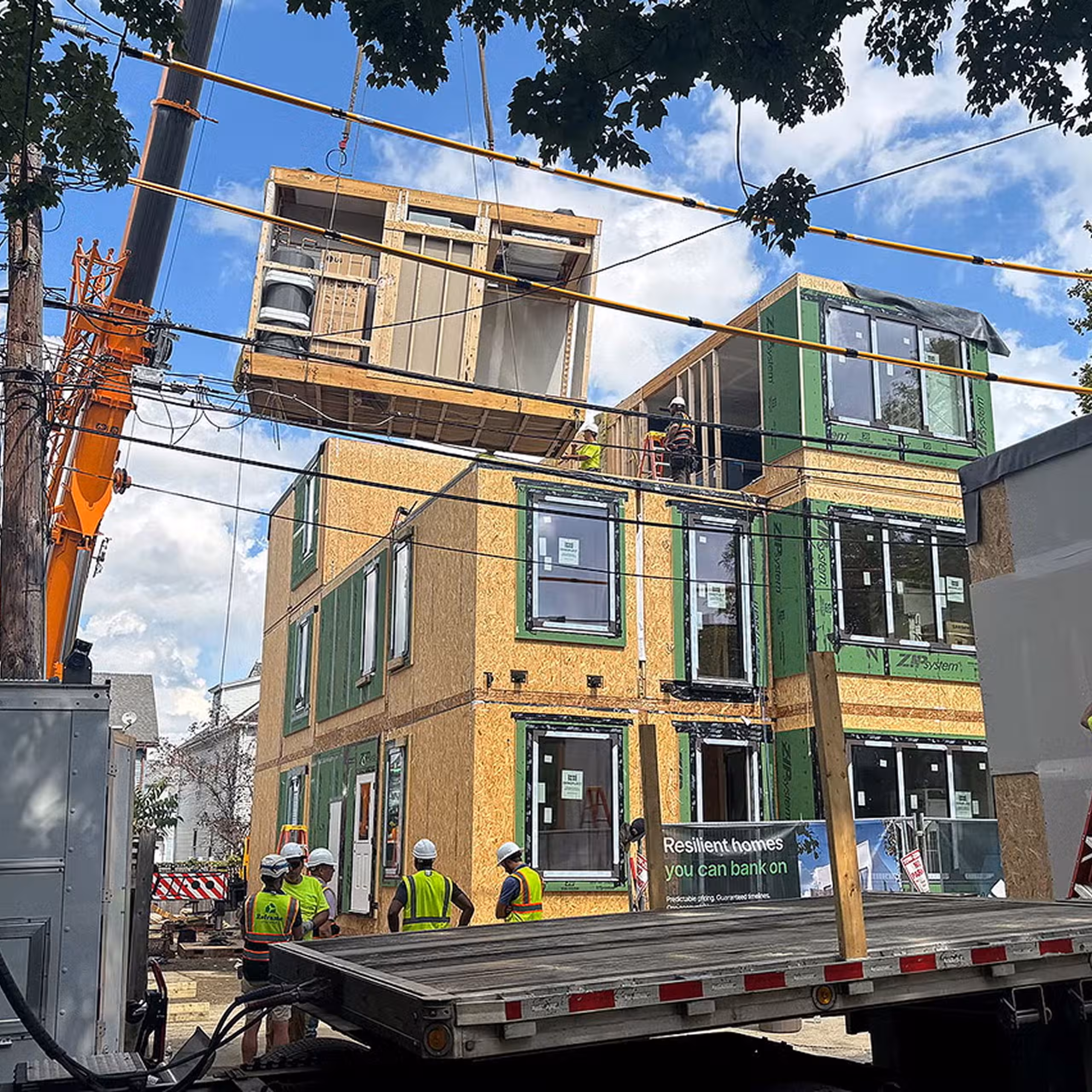 Crane stacking modular building sections between existing homes during assembly