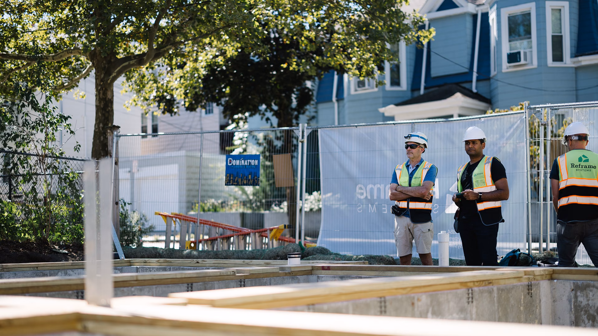 Reframe Systems workers in safety vests standing at a fenced residential build site
