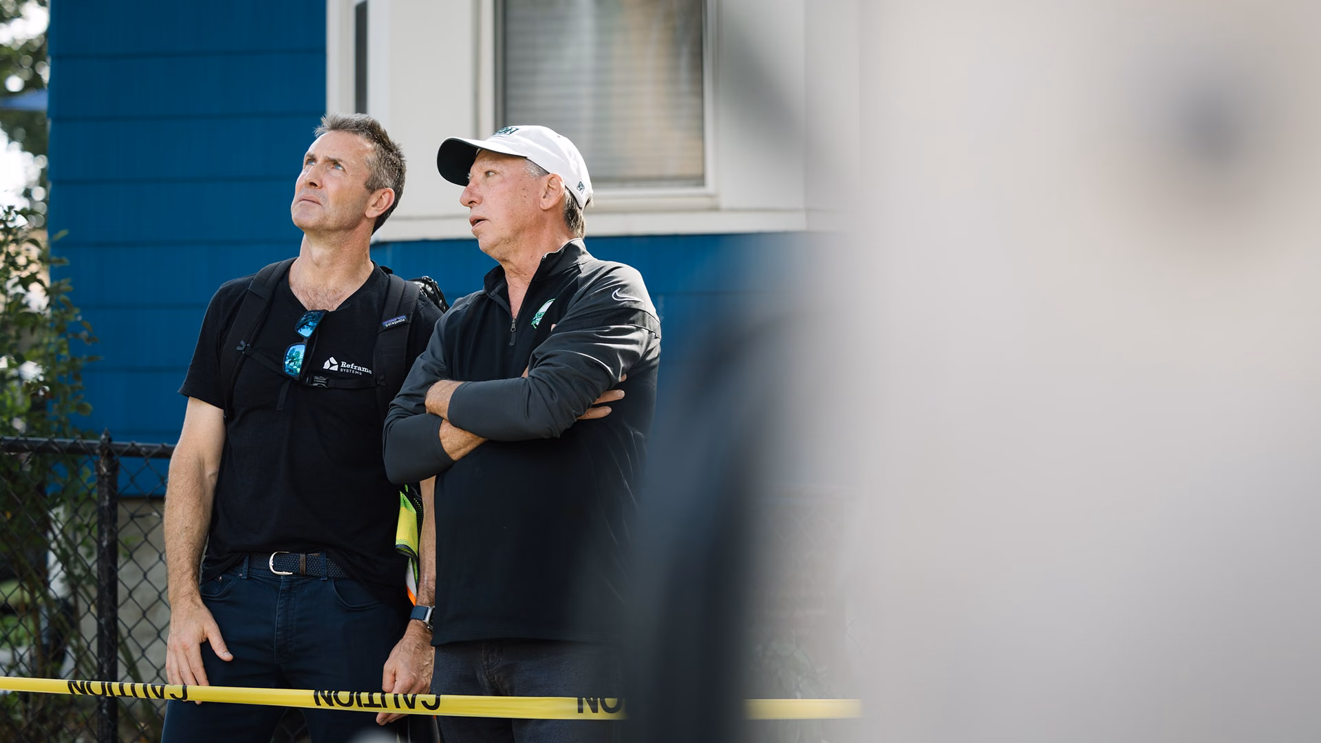 Two Reframe Systems team members looking up at a building behind caution tape on site