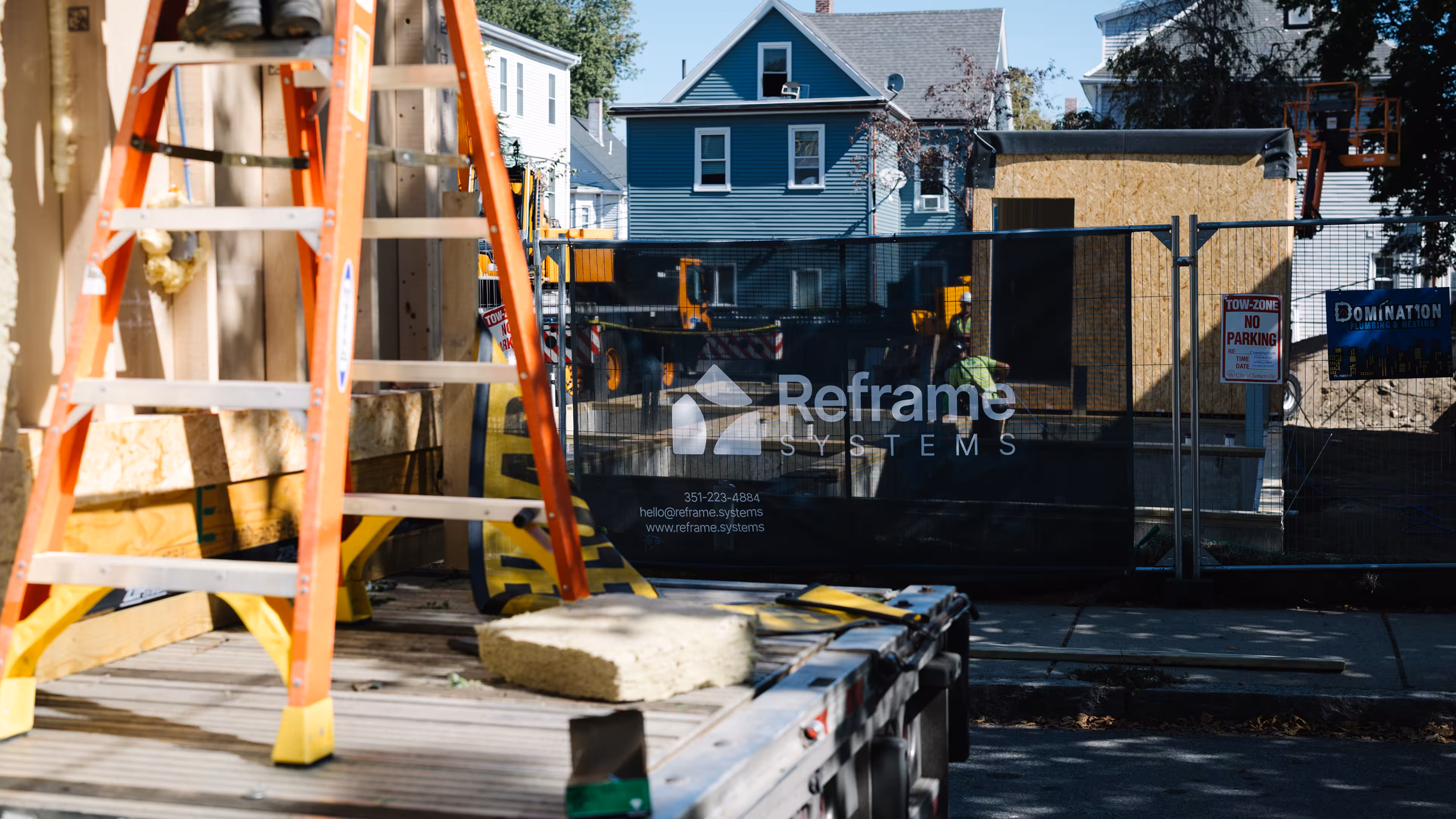 Reframe Systems banner on site fencing in front of a blue multi-family home during construction