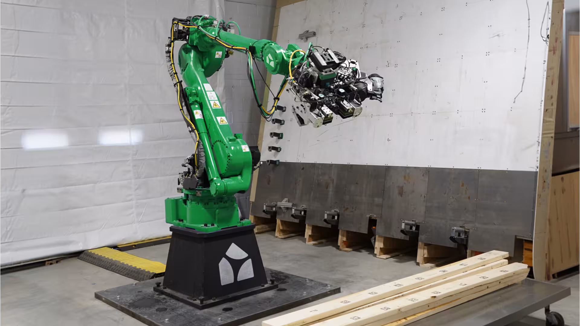 Green robotic arm handling a tool head beside framing lumber in the Reframe Systems microfactory