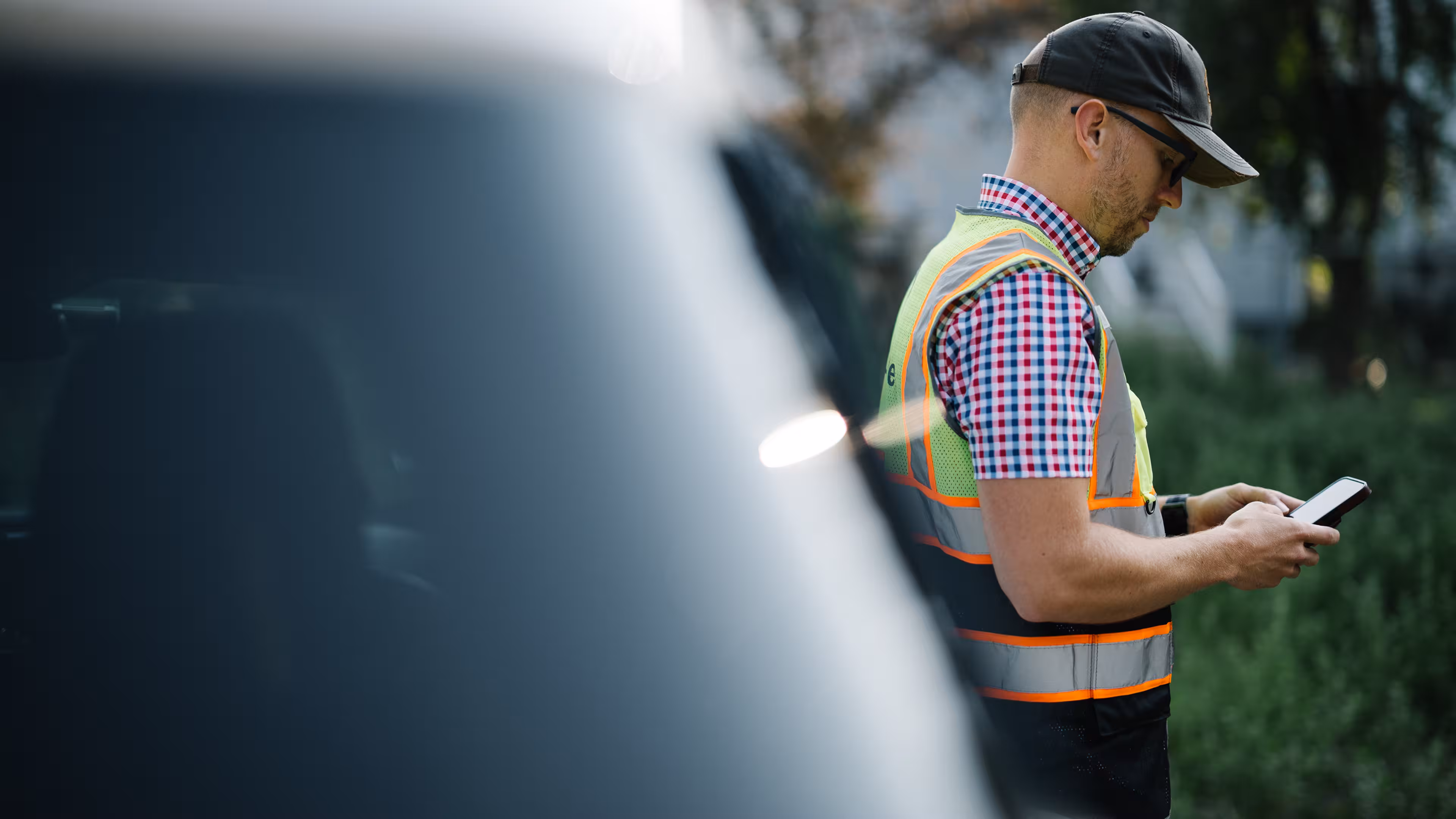 Reframe Systems worker in a safety vest checking a phone beside a vehicle outdoors