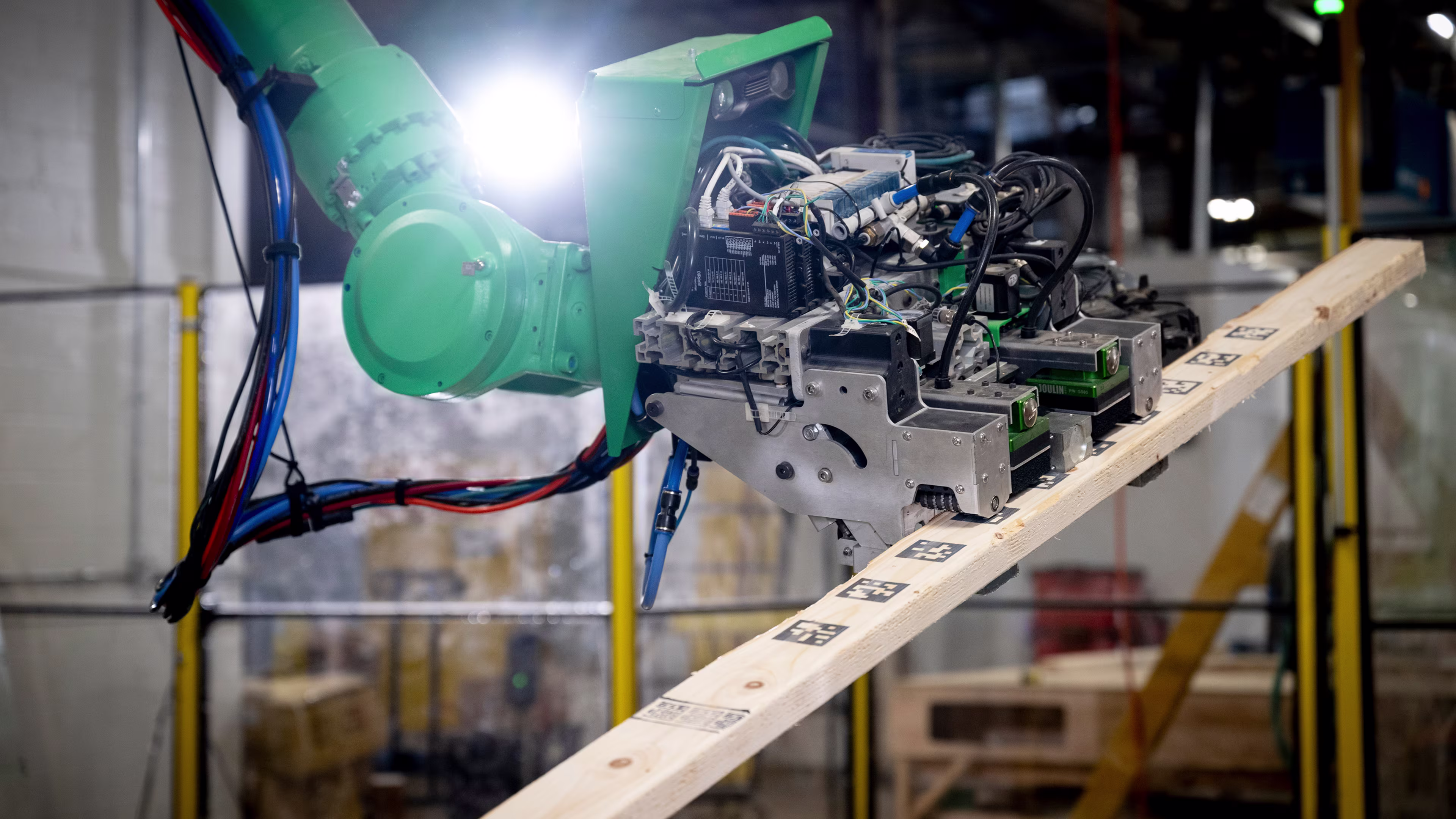 Green robotic arm processing a length of lumber on a track in the Reframe Systems microfactory