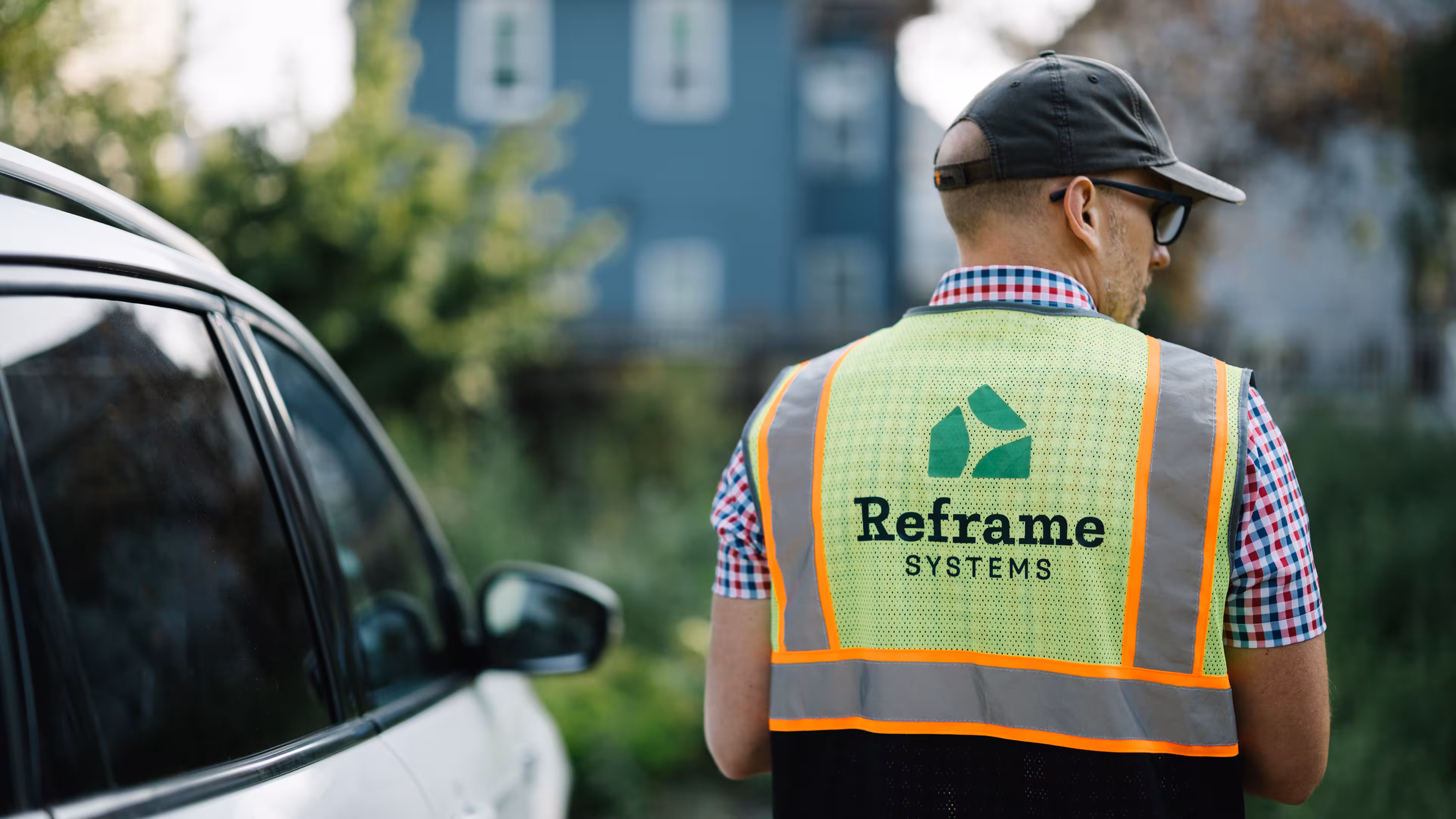 A Reframe Systems team member in a high-visibility vest standing in front of a residential home on a job site.